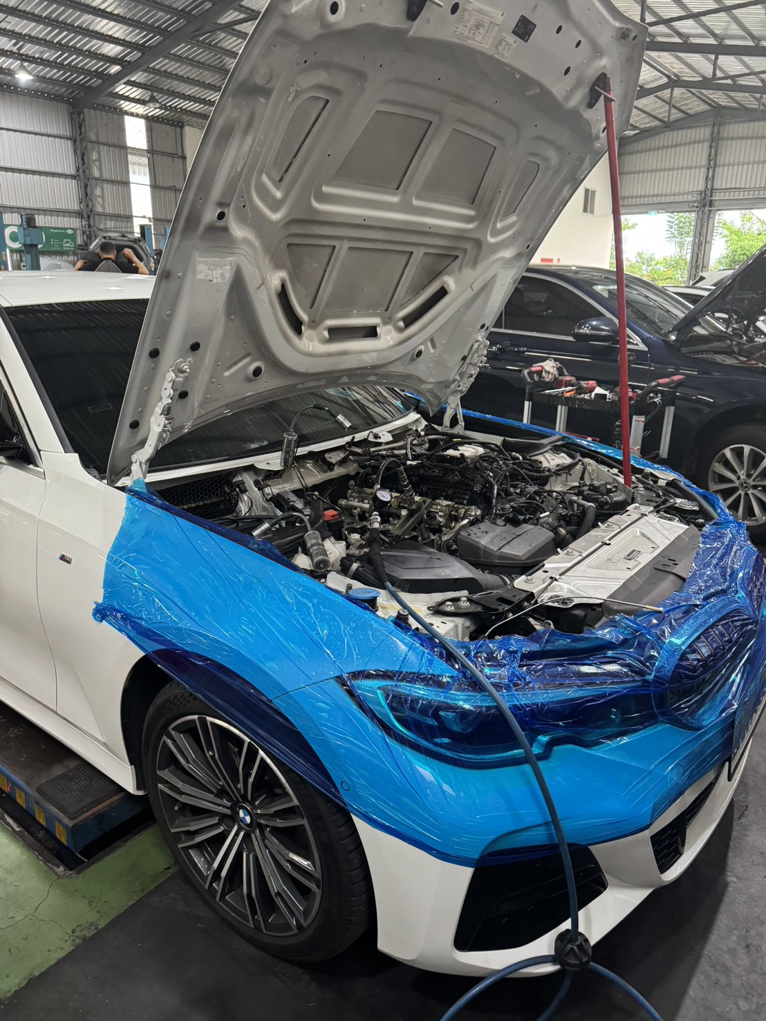 BMW 320i 前艙以藍色保護膜完整包覆，準備拆解引擎頂部